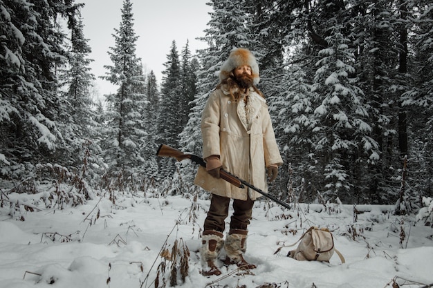 Hunter in vintage clothes with gun sneaks through forest