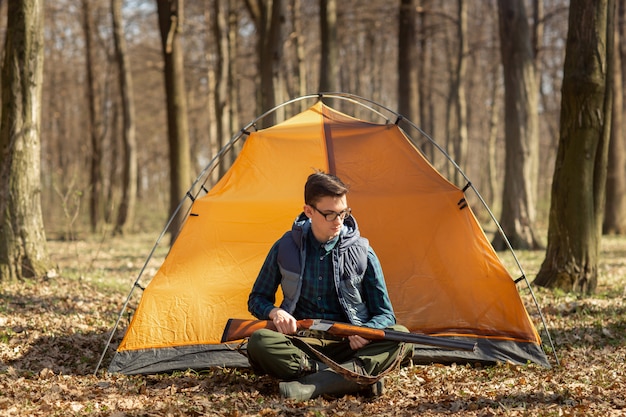 Hunter with a gun in the forest sitting near the tent