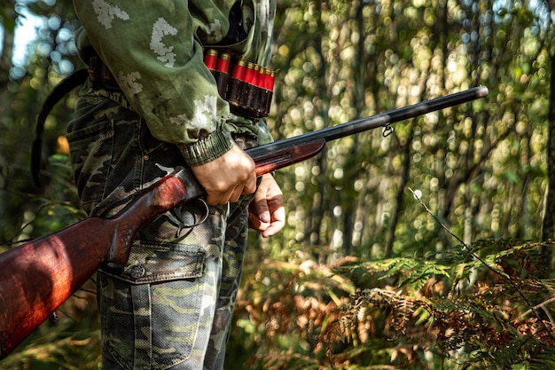 Hunter with a gun in his hands in hunting clothes in the autumn forest 