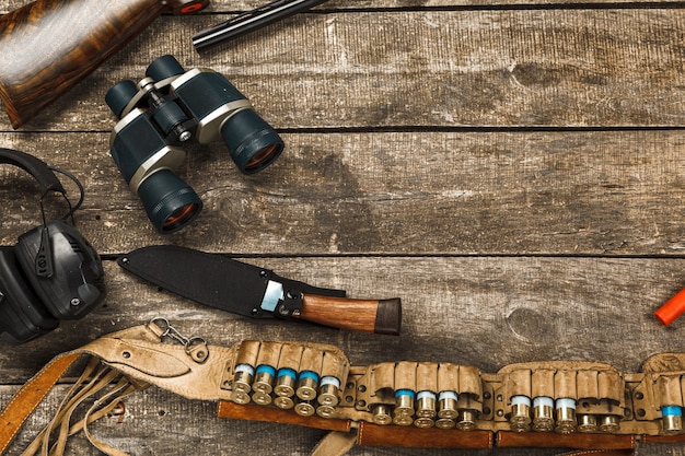 Hunting equipment on old wooden background including rifle knife binoculars and cartridges