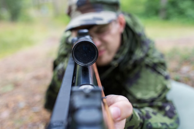 hunting, war, army and people concept - close up of young soldier, ranger or hunter with gun in forest