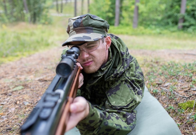 hunting, war, army and people concept - close up of young soldier, ranger or hunter with gun in forest