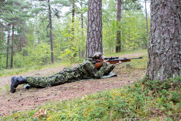 hunting, war, army and people concept - young soldier, ranger or hunter with gun in forest