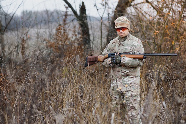 Hunting, war, army and people concept - young soldier, ranger or hunter with gun walking in forest