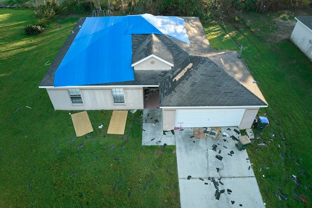 Hurricane Ian damaged house rooftop covered with protective plastic tarp against rain water leaking until replacement of asphalt shingles Aftermath of natural disaster