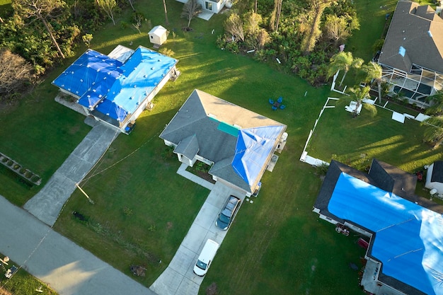 Hurricane Ian damaged house rooftops covered with protective plastic tarp against rain water leaking until replacement of asphalt shingles Aftermath of natural disaster