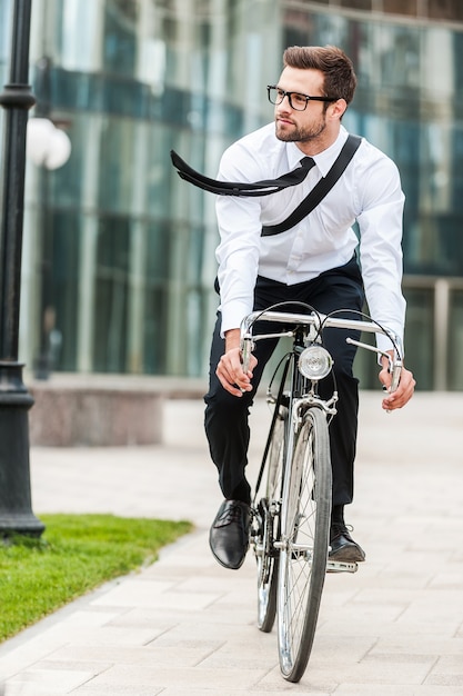 Hurrying to office. Full length of handsome young businessman looking away while riding on his bicycle