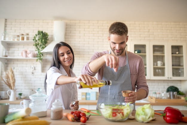 Husband adding spices to salad while cooking with wife in the morning