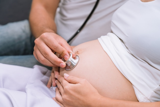 Husband excited use a stethoscope listen to sound of baby in belly his pregnant wife