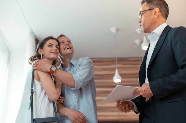 Husband hugging wife after buying house standing near realtor