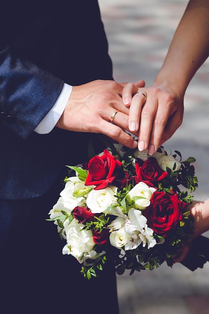 husband and wife hands with wedding rings on a bouquet of rose