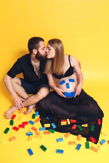 Husband and wife play children's constructor Pregnant girl shows emoji from the constructor on her stomach