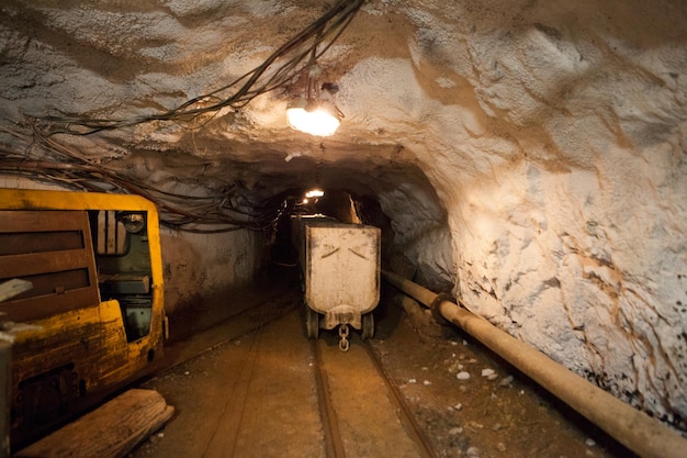 Hutch cart with raw material standing at underground mining. Production and technology concept. Tunnel with railway and electricity mine cables of underground mining. Transportation and lighting.