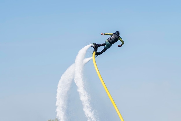 Hydrofyler jet boots operation Young man riding flyboard jetski on water Summer fun activity Hydro flying jetpack board attached to water craft