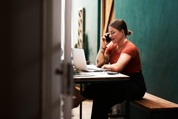 Photo i always follow up on my clients cropped shot of an attractive young businesswoman sitting alone and using her cellphone while using her laptop