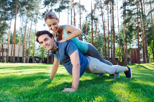 I believe in you. Joyful young woman smiling while helping her boyfriend to do push ups