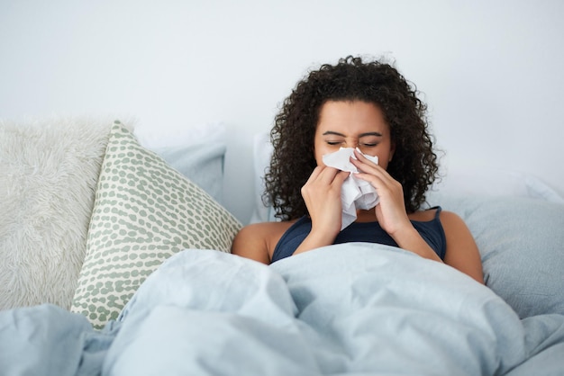 I definitely cant go to work with this cold Shot of an attractive young woman feeling sick and blowing her nose while in bed in the morning