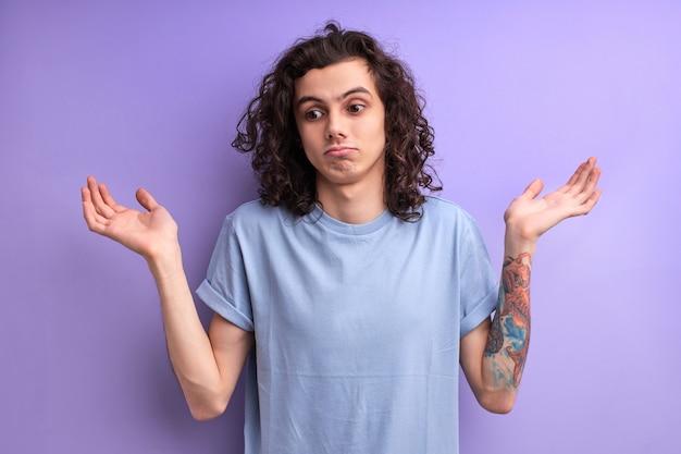 I dont know portrait of confused handsome young male in blue casual tshirt standing with raised arms...