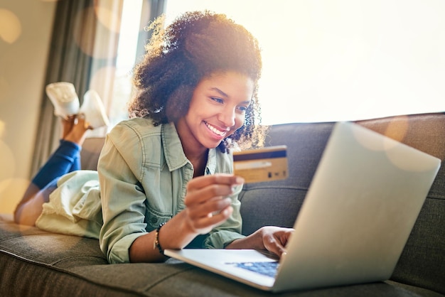 I have the power of the card in my hand Shot of a cheerful young woman doing online shopping while lying on a couch at home during the day