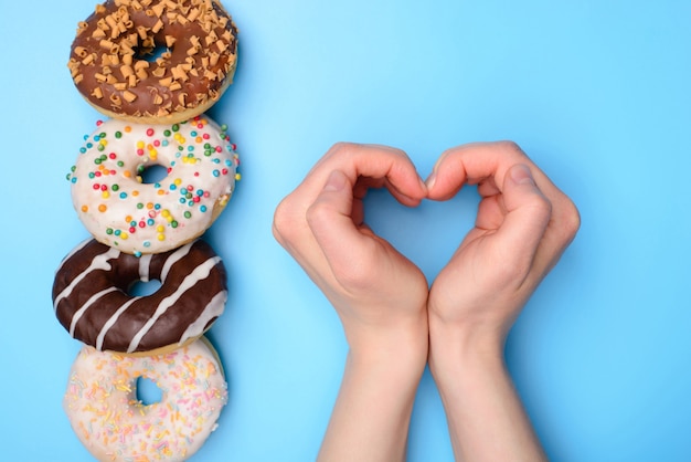 I love eating donuts concept. Flat lay top overhead view photo of four food objects lying in a row and person kid child making heart with hands isolated pastel background