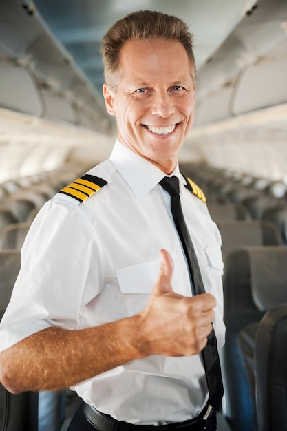 Photo i love my job! confident male pilot in uniform showing his thumb up and smiling