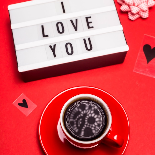 I love you written in black letters on a decorative lamp next to a red espresso cup 