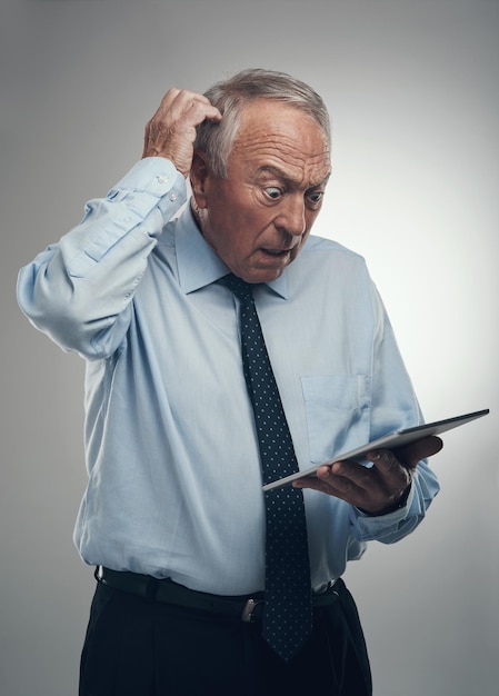 I missed an appointment with my investors Shot of a senior businessman standing alone against a grey studio background and looking confused while using a digital tablet