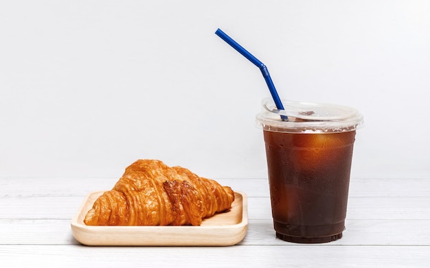 Ice americano coffee in a cup with croissant on wooden plate ready for breakfast meal