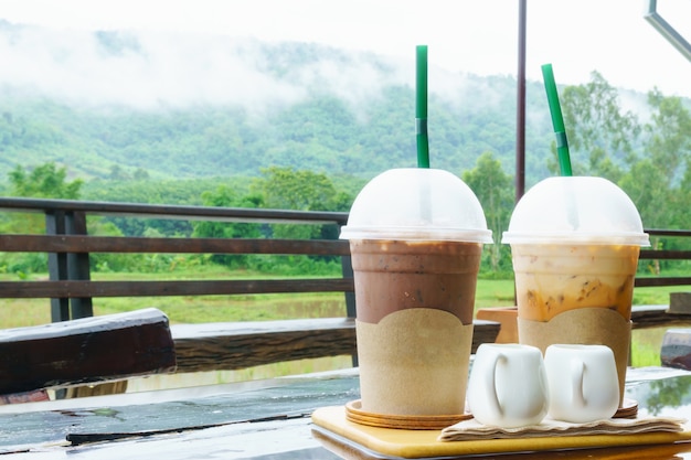 Ice Cocoa and ice milk tea on the table with mountain scenery and mist in rainny day