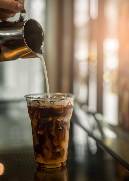 Ice coffee on a plastic cup with cream being poured into it showing the texture