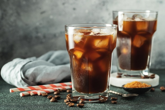 Ice coffee in a tall glass with cream poured over ice cubes and beans on a dark concrete table