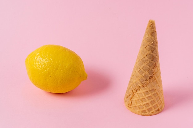 Ice cream cone and lemon fruit on a light pink background.