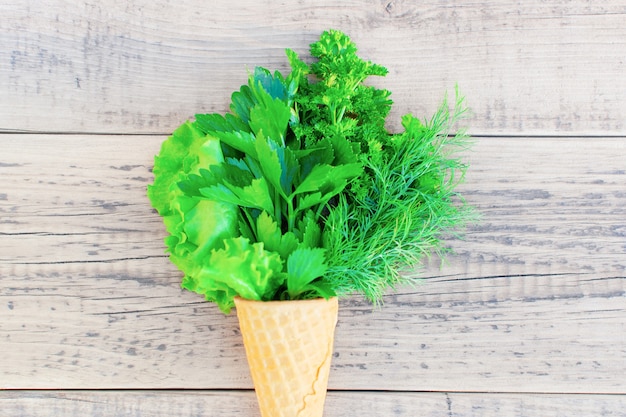 Ice cream cone with fresh herbs on a wooden. Lettuce, parsley, dill, garlic flower. 