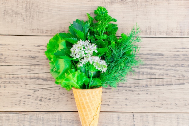 Ice cream cone with fresh herbs on a wooden. Lettuce, parsley, dill, garlic flower. 