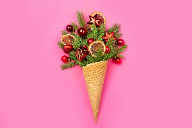 Ice cream cone with twigs of Christmas tree and toys on a pink.