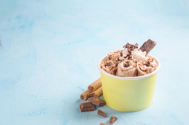 Ice cream roll of chocolate and coffee, with pieces of chocolate and cookies on blue background