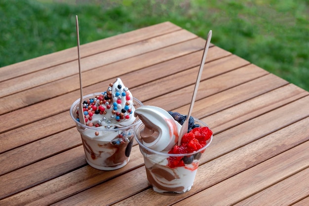 Ice cream with berries in plastic cups on wooden table Street food sweets refreshing summer snack