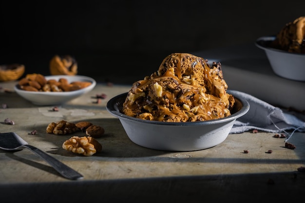 Ice cream with chocolate, nuts and almonds served in metal bowl on wooden table.