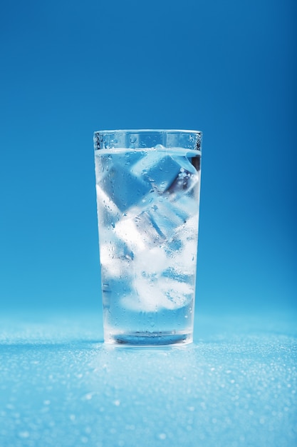 Ice cubes in a glass with crystal clear water on a blue surface