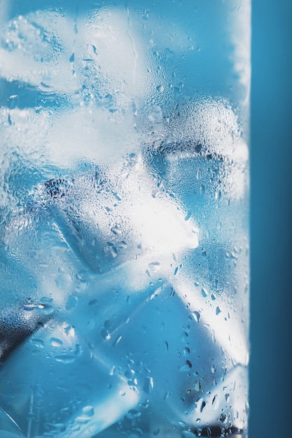 Ice cubes in a glass with refreshing ice water on a blue background. Close-up