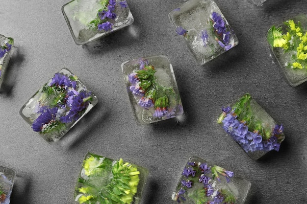 Ice cubes with flowers on grey stone background flat lay