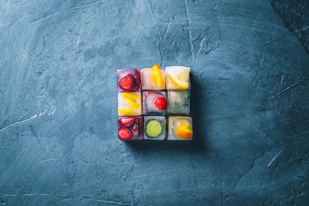 Ice cubes with fruit on a stone blue surface. The shape of the square. Mint, strawberry, cherry, lemon, orange. flat lay, top view