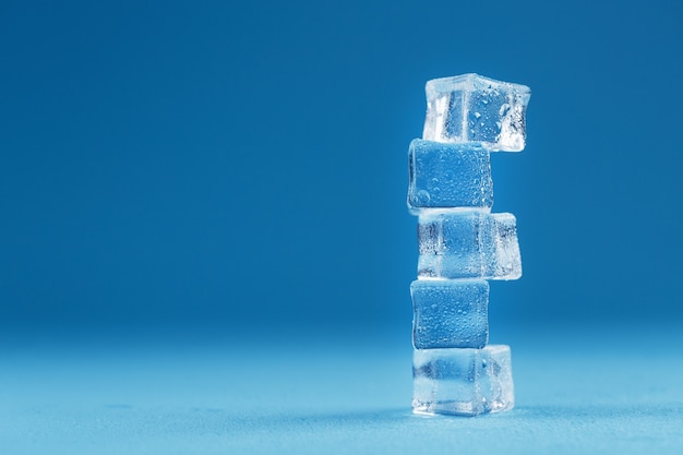 Ice cubes with water drops tower in a row on a blue background.