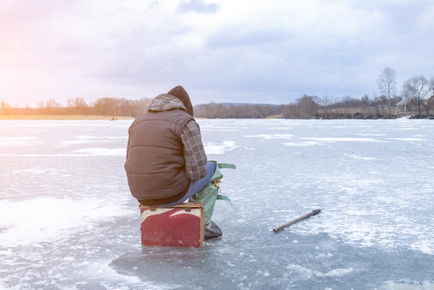 Ice fishing on ice a fisherman sits on a fishing chest and catches fish on a frozen lake