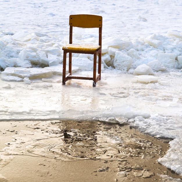 Icebound chair on edge of icehole in frozen lake