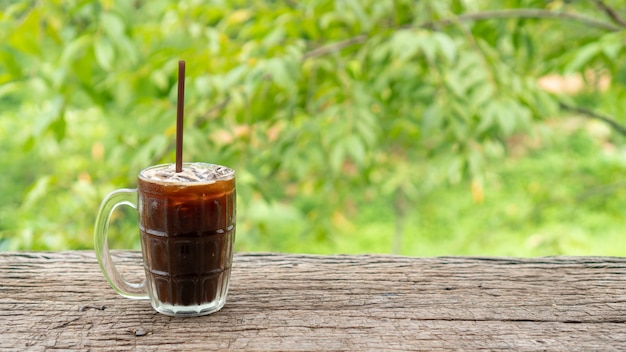 Iced Americano coffee on a wooden table and green nature 