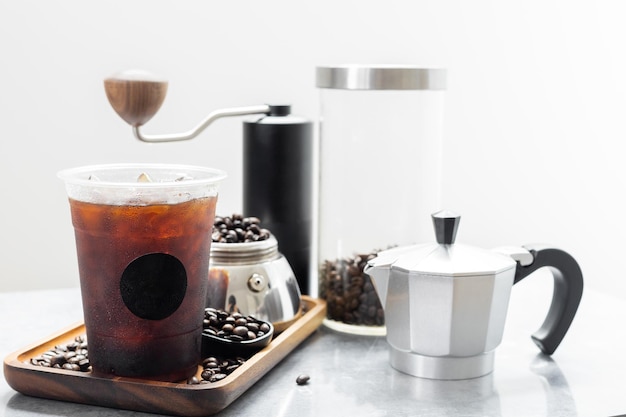 Iced black coffee in plastic cup with black logo sticker on wooden tray Americano from moka pot style italian