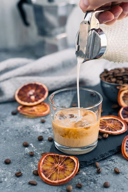 Iced coffee with milk Summer drink Pouring milk in coffee with ice cube on grey background