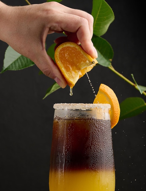 Iced coffee with orange juice in a transparent glass a woman's hand squeezes an orange slice into a bubble drink