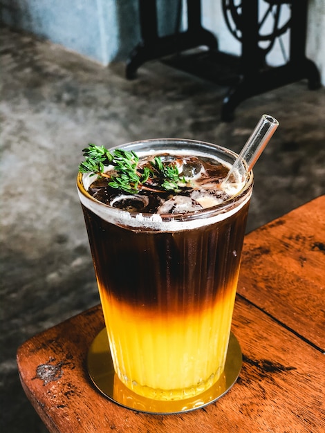 Iced fresh orange juice topped with espresso on wooden table in Modern cafe.